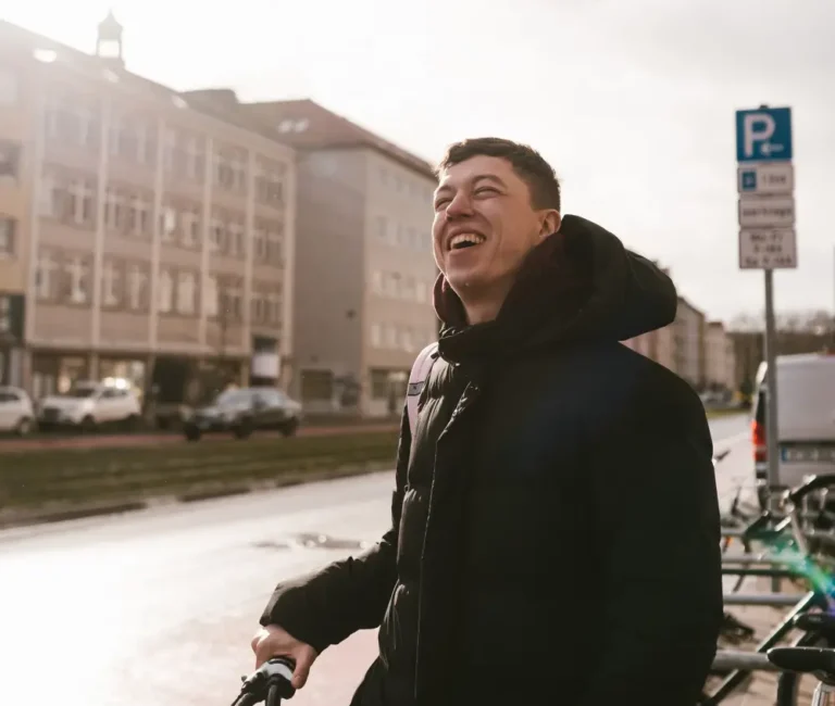 photo-of-man-in-winter-jacket-looking-up-at-sun-on-cloudy-day-with-dutch-buildings-and-canal-in-background